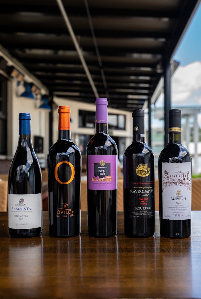 A variety of wine bottles arranged on a wooden table in an outdoor setting.