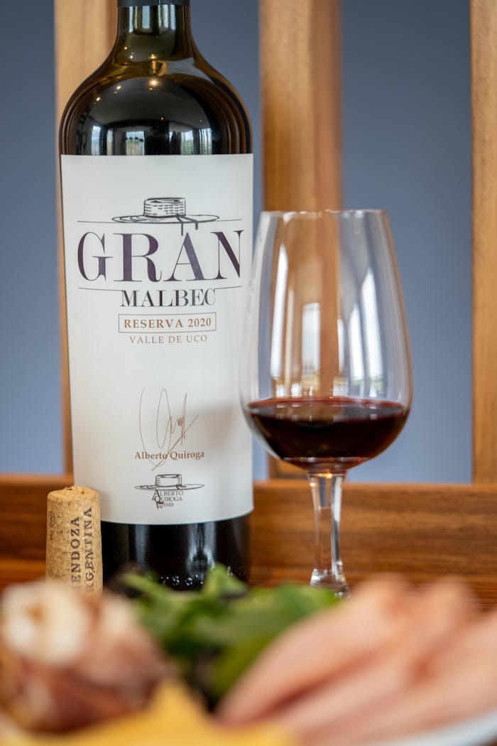 Gran Malbec wine bottle and glass of red wine on wooden table with cork.