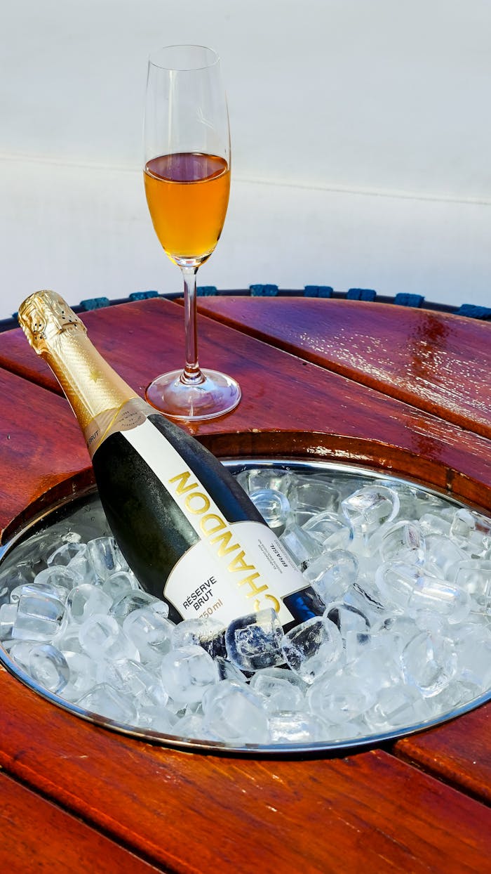 Elegant champagne bottle on ice beside filled flute on a polished wooden table, ready for celebration.
