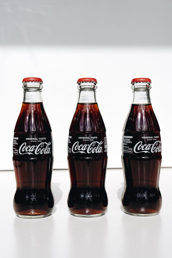 Three classic Coca-Cola glass bottles in a well-lit, minimalist setting.