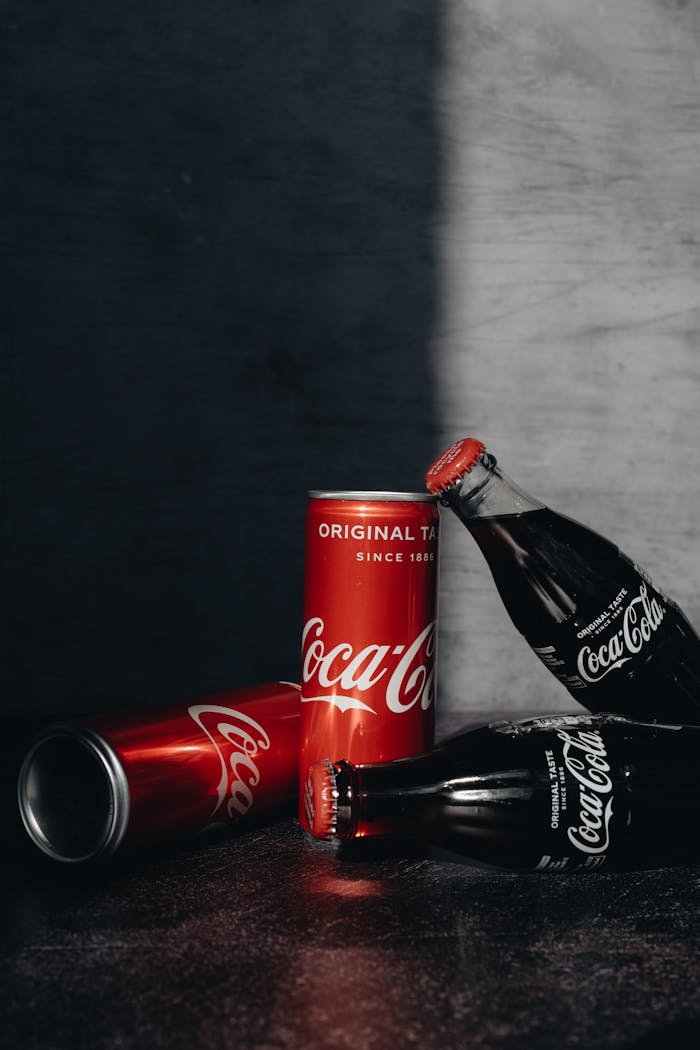 Artistic still life featuring Coca-Cola bottles and can on a dark background, highlighting the brand's iconic design.