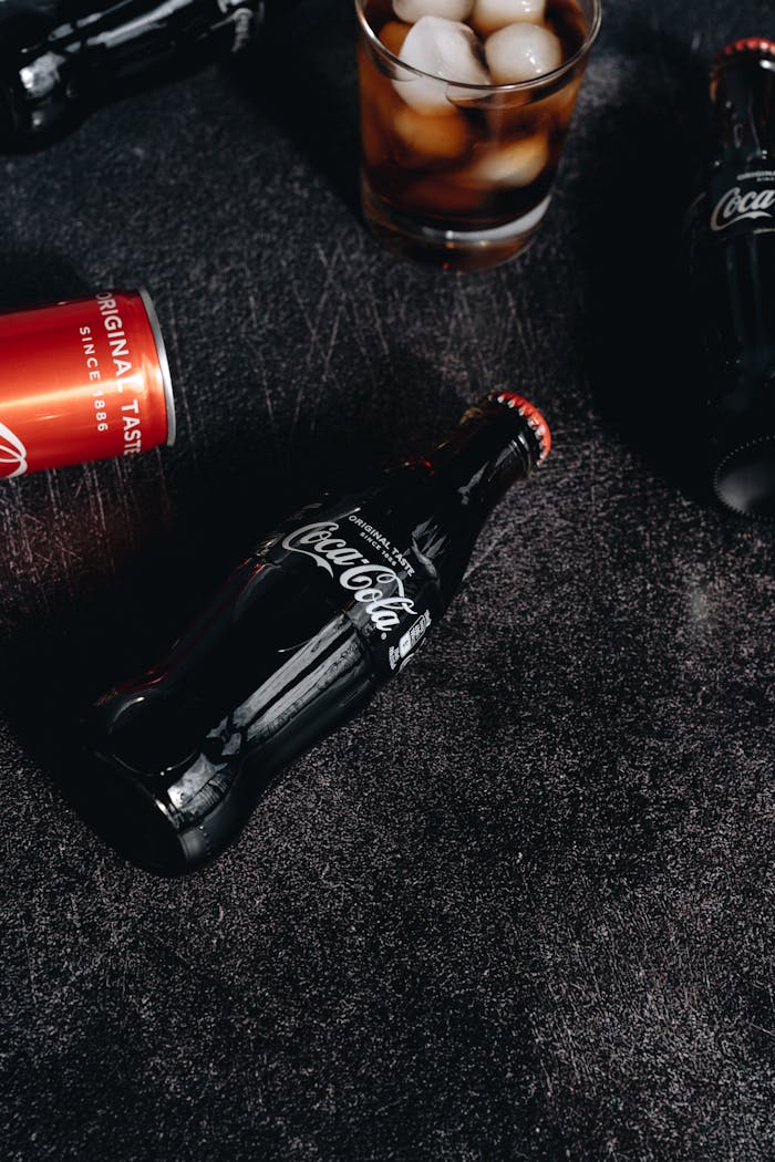 Close-up of Coca-Cola bottles and a drink with ice cubes, showcasing refreshment and classic taste.