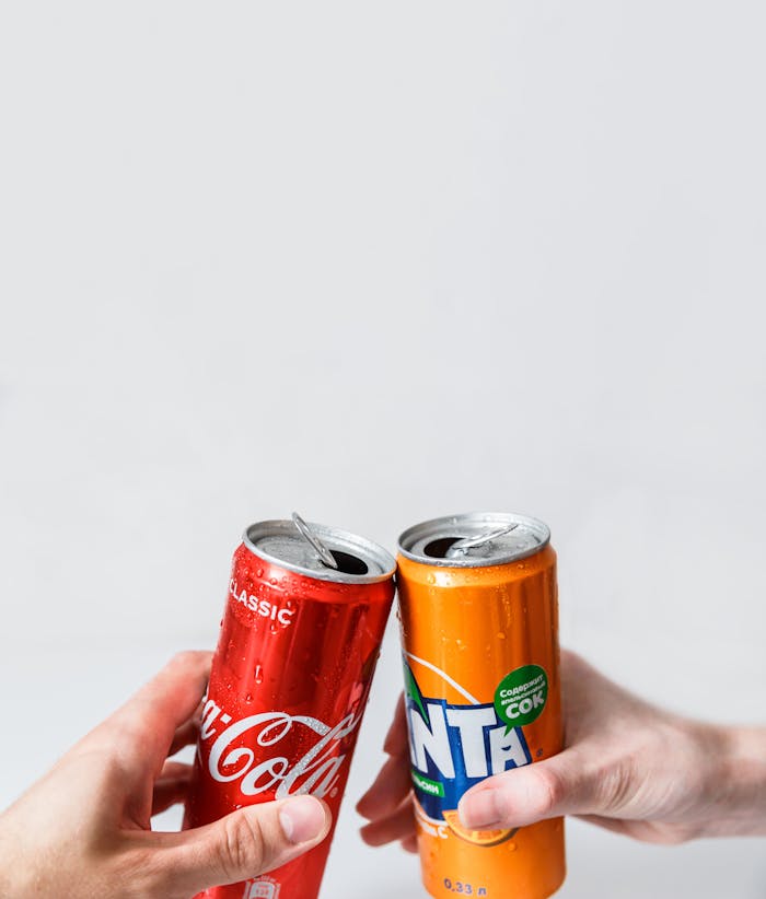 Close-up of hands toasting with Coca-Cola and Fanta cans, conveying a sense of refreshment and celebration.